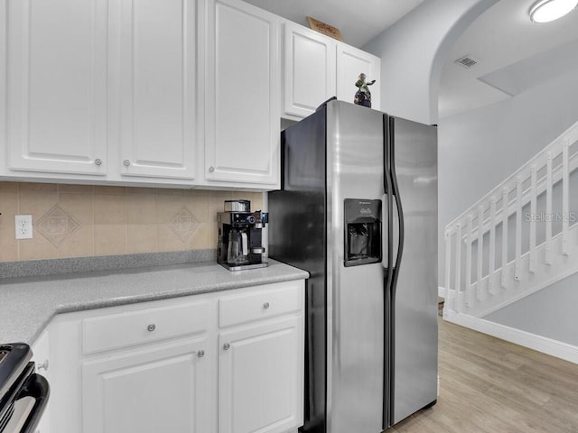 kitchen with decorative backsplash, stainless steel refrigerator with ice dispenser, stove, light hardwood / wood-style flooring, and white cabinets