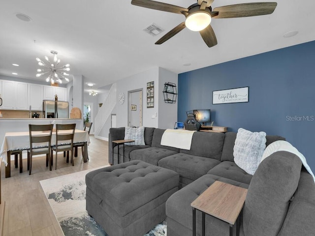 living room with ceiling fan with notable chandelier and light wood-type flooring