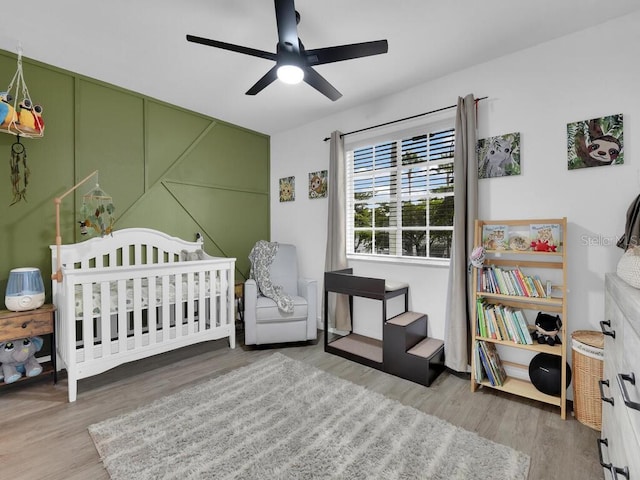 bedroom with a crib, hardwood / wood-style flooring, and ceiling fan