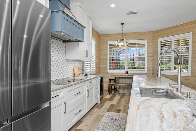 kitchen with stainless steel refrigerator, white cabinetry, sink, pendant lighting, and black electric stovetop