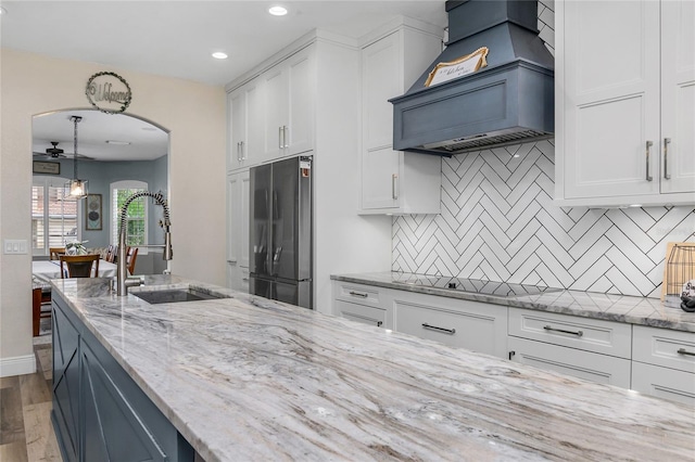 kitchen with white cabinets, premium range hood, stainless steel refrigerator, and sink