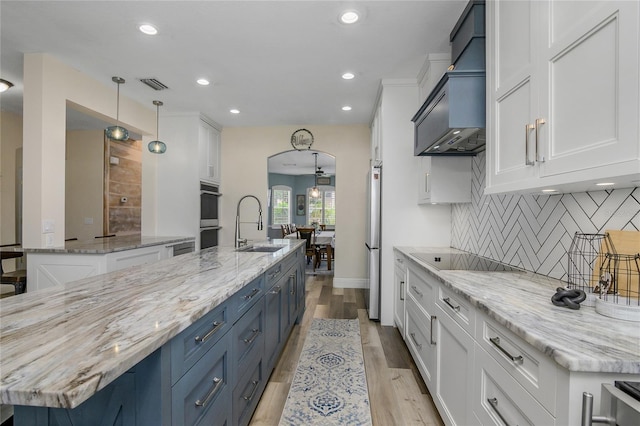 kitchen with a large island, white cabinetry, light stone counters, decorative light fixtures, and custom range hood