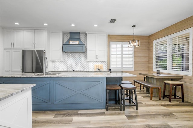 kitchen with premium range hood, light stone counters, white cabinets, hanging light fixtures, and a breakfast bar area