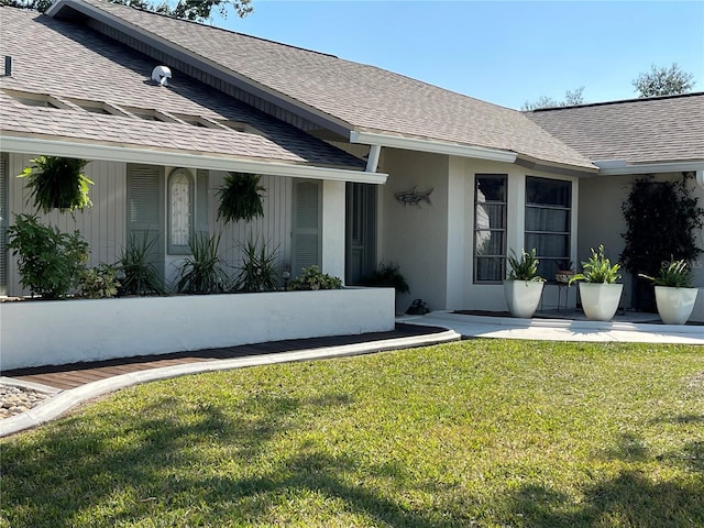 doorway to property featuring roof with shingles, a lawn, and stucco siding