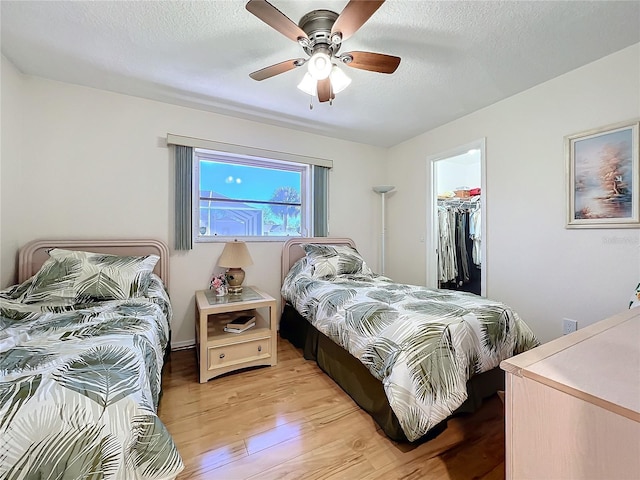 bedroom featuring ceiling fan, light hardwood / wood-style flooring, a textured ceiling, a walk in closet, and a closet