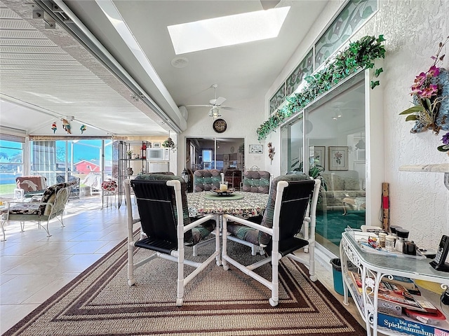 dining room featuring tile patterned floors, ceiling fan, and lofted ceiling with skylight