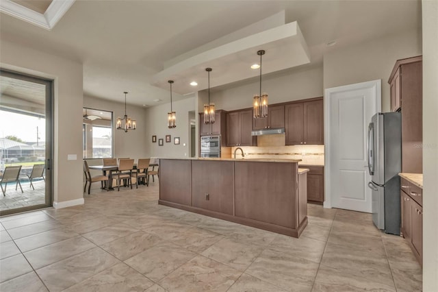 kitchen featuring stainless steel refrigerator, an inviting chandelier, backsplash, an island with sink, and pendant lighting