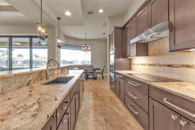 kitchen with light stone countertops, tasteful backsplash, black electric cooktop, sink, and decorative light fixtures