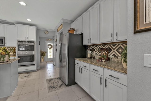 kitchen with backsplash, white cabinets, light tile patterned floors, and appliances with stainless steel finishes