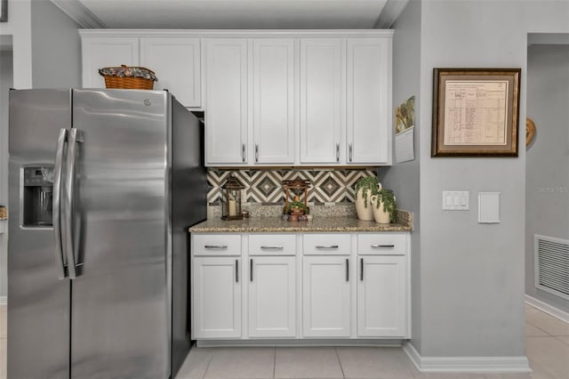 kitchen with light stone countertops, stainless steel refrigerator with ice dispenser, tasteful backsplash, white cabinetry, and light tile patterned flooring