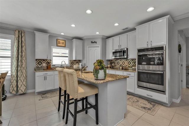 kitchen featuring backsplash, white cabinets, an island with sink, and stainless steel appliances