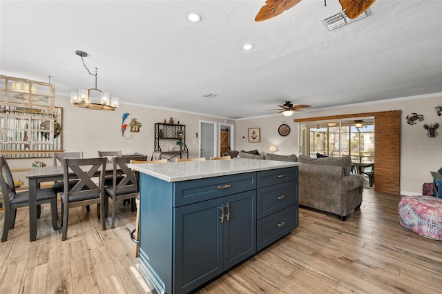 kitchen with a center island, ceiling fan with notable chandelier, blue cabinets, crown molding, and light wood-type flooring