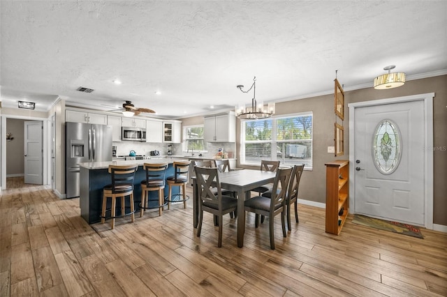 dining space with light hardwood / wood-style floors, ceiling fan with notable chandelier, and ornamental molding