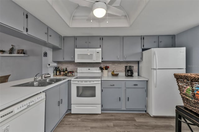 kitchen featuring decorative backsplash, white appliances, a tray ceiling, sink, and gray cabinets