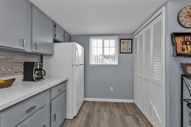 kitchen with gray cabinets, decorative backsplash, white fridge, and light hardwood / wood-style floors