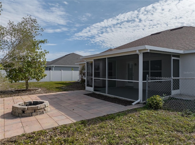 back of property featuring a lawn, a sunroom, a patio, and an outdoor fire pit