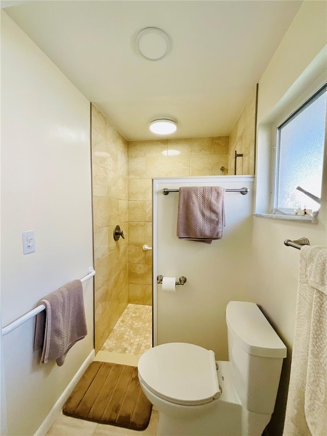 bathroom featuring tile patterned flooring, a tile shower, and toilet