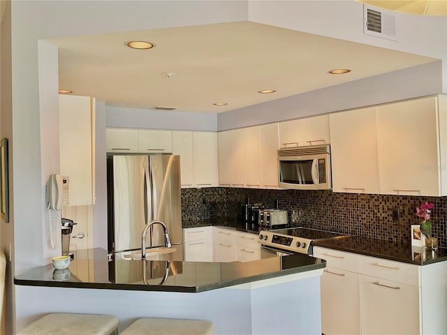 kitchen with kitchen peninsula, appliances with stainless steel finishes, a breakfast bar, sink, and white cabinetry