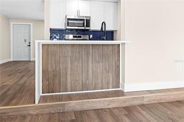 kitchen featuring white cabinets, sink, hardwood / wood-style flooring, tasteful backsplash, and range