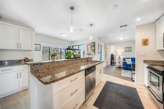 kitchen with stainless steel appliances, a kitchen island with sink, sink, pendant lighting, and white cabinets