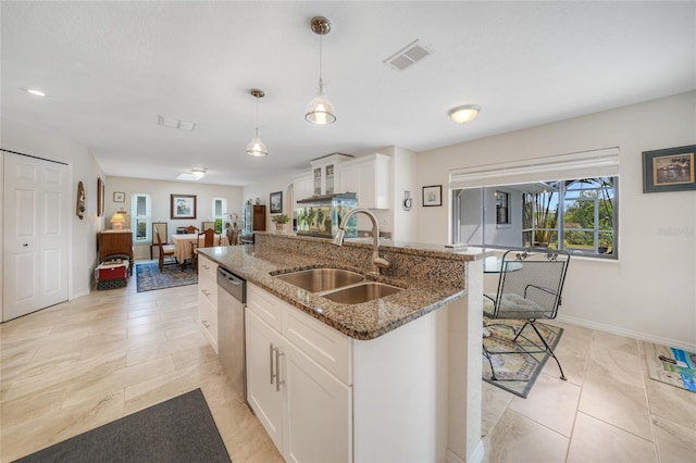 kitchen with a kitchen island with sink, sink, hanging light fixtures, stainless steel dishwasher, and white cabinetry