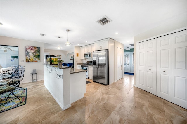 kitchen featuring white cabinets, hanging light fixtures, a breakfast bar area, dark stone countertops, and stainless steel appliances