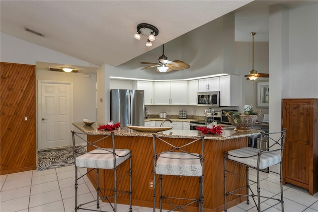 kitchen featuring ceiling fan, light stone countertops, appliances with stainless steel finishes, white cabinetry, and a breakfast bar area