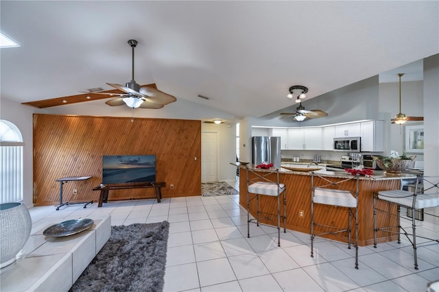 kitchen with kitchen peninsula, lofted ceiling, wooden walls, white cabinets, and appliances with stainless steel finishes