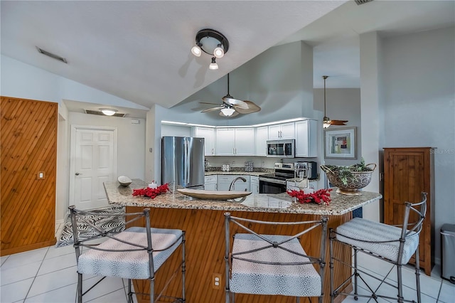 kitchen featuring stainless steel appliances, vaulted ceiling, ceiling fan, light tile patterned floors, and white cabinetry