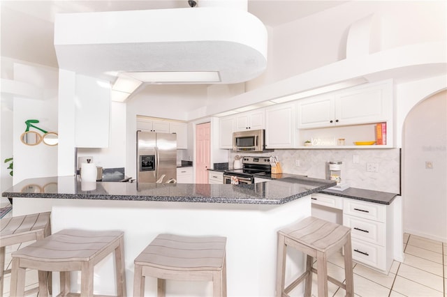 kitchen with light tile patterned floors, a kitchen breakfast bar, kitchen peninsula, white cabinets, and appliances with stainless steel finishes