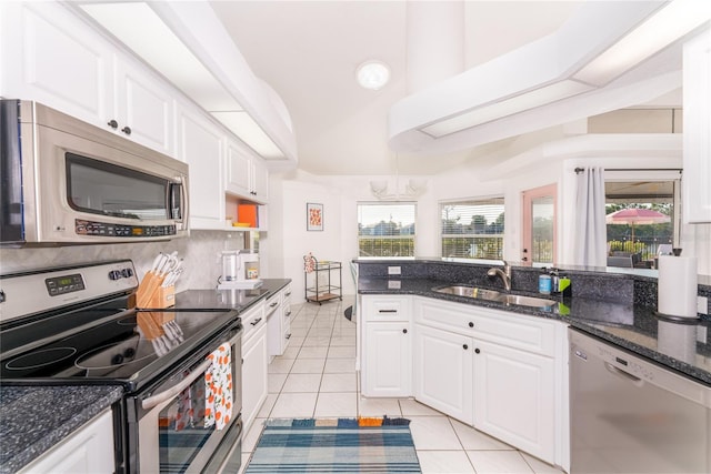 kitchen with dark stone counters, stainless steel appliances, sink, light tile patterned floors, and white cabinets