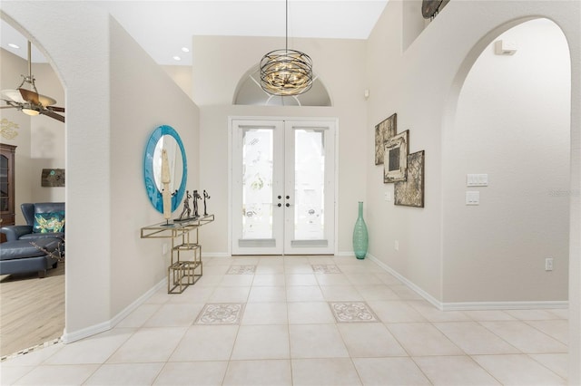 tiled entrance foyer with ceiling fan with notable chandelier, a high ceiling, and french doors