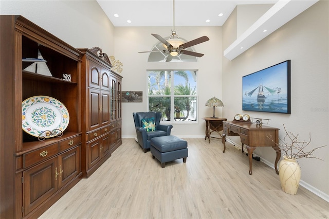 living area with ceiling fan, light wood-type flooring, and a towering ceiling