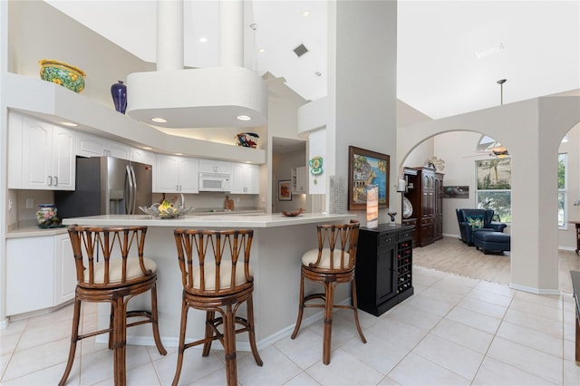 kitchen featuring kitchen peninsula, stainless steel refrigerator with ice dispenser, a kitchen breakfast bar, a high ceiling, and white cabinetry