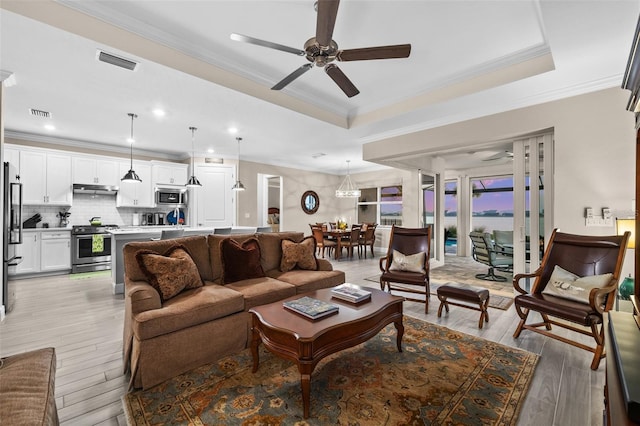 living room with a tray ceiling, crown molding, and ceiling fan