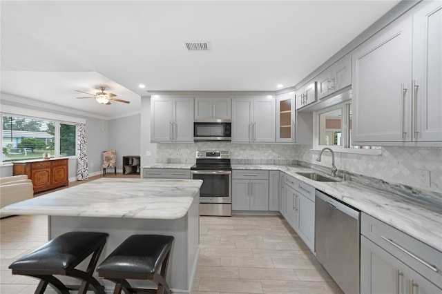 kitchen with gray cabinetry, sink, light stone counters, a breakfast bar, and appliances with stainless steel finishes