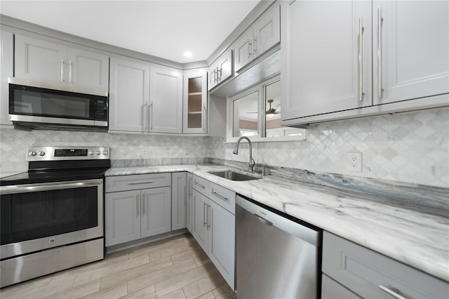 kitchen with gray cabinets, light stone counters, sink, and appliances with stainless steel finishes