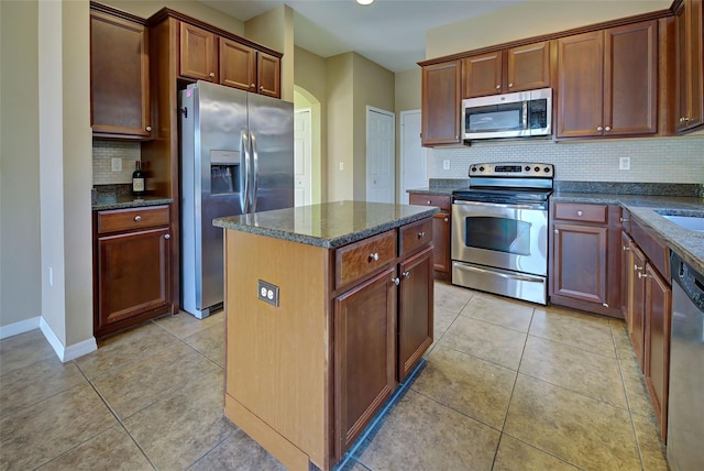 kitchen featuring a center island, backsplash, dark stone counters, light tile patterned flooring, and stainless steel appliances