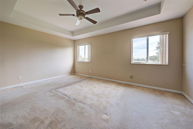 carpeted spare room with a tray ceiling, ceiling fan, and a healthy amount of sunlight