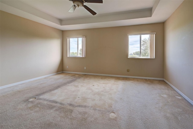 carpeted empty room with a raised ceiling and ceiling fan