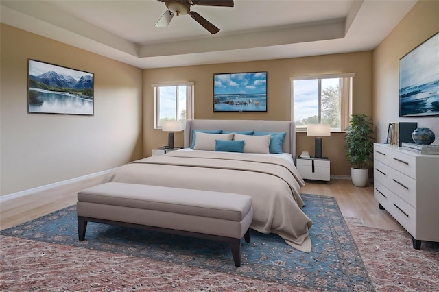 bedroom featuring multiple windows, a raised ceiling, light hardwood / wood-style flooring, and ceiling fan