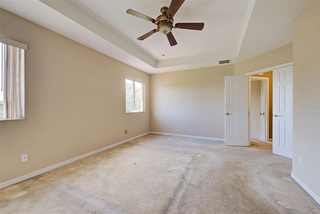 empty room featuring light carpet, a tray ceiling, and ceiling fan