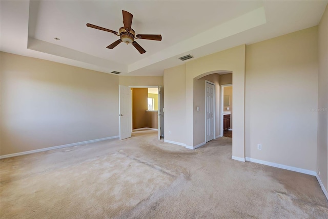 carpeted spare room with ceiling fan and a tray ceiling