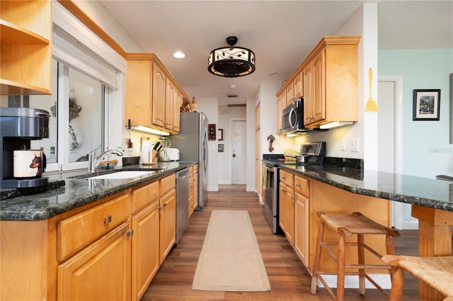 kitchen with sink, stainless steel appliances, kitchen peninsula, dark stone countertops, and wood-type flooring