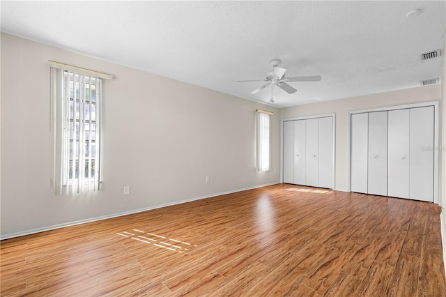 unfurnished bedroom with a textured ceiling, light hardwood / wood-style flooring, ceiling fan, and multiple closets