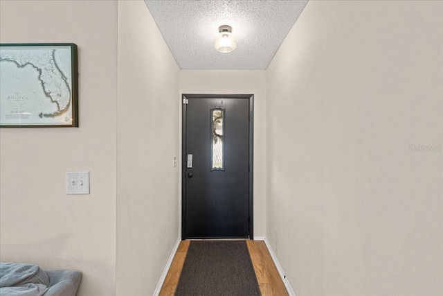 doorway to outside featuring a textured ceiling, wood finished floors, and baseboards