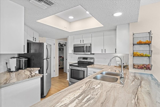 kitchen featuring a textured ceiling, stainless steel appliances, a sink, and white cabinets