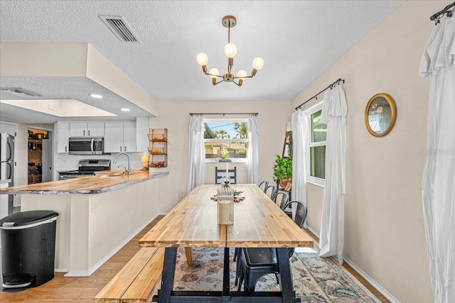 dining area with sink, light wood-type flooring, a textured ceiling, and a notable chandelier