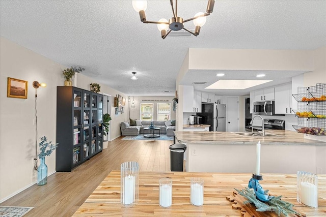 dining room with light hardwood / wood-style floors, sink, a textured ceiling, and an inviting chandelier