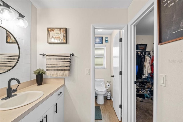 bathroom with toilet, a spacious closet, wood finished floors, and vanity